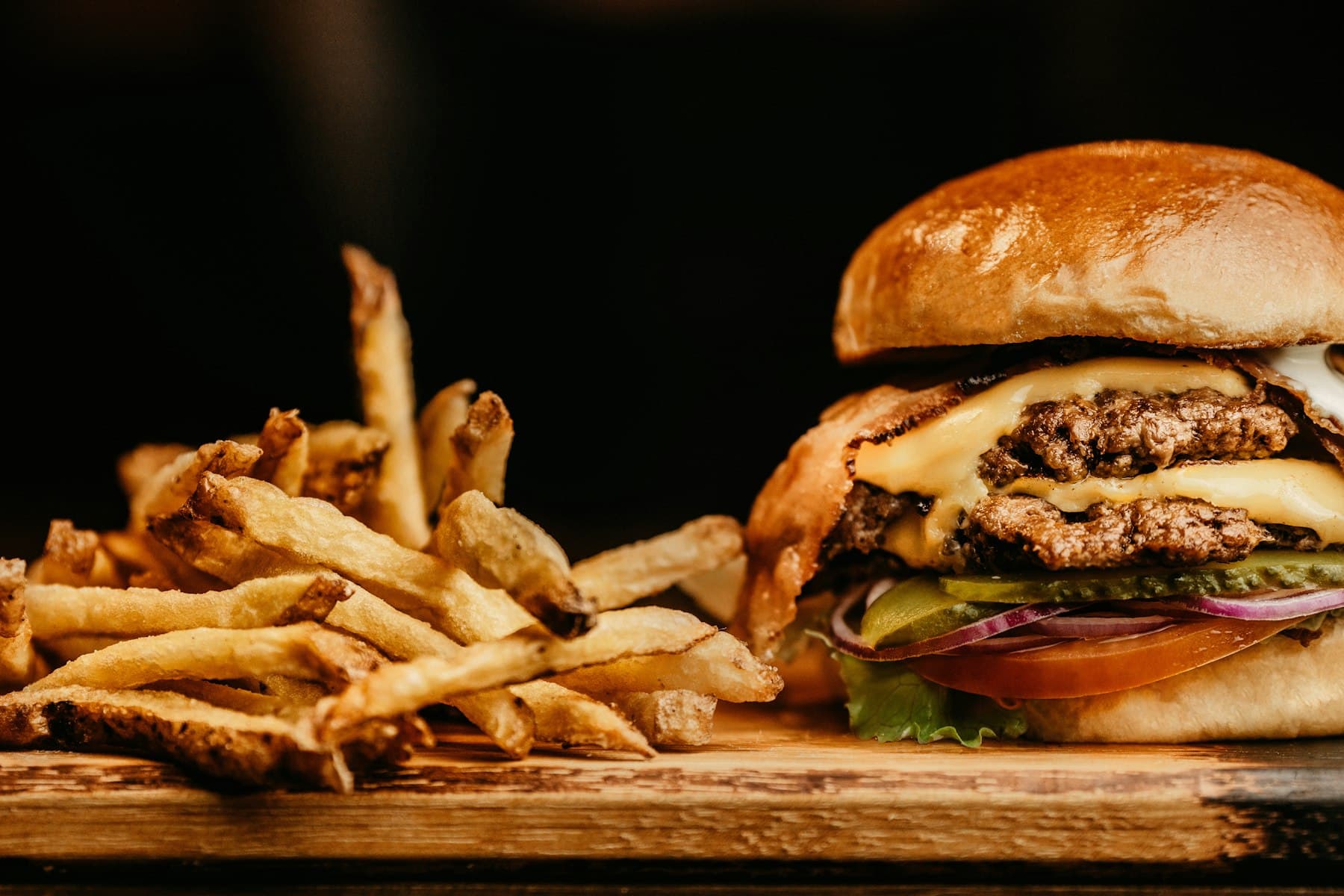 Burger maison servi avec des frites sur une planche